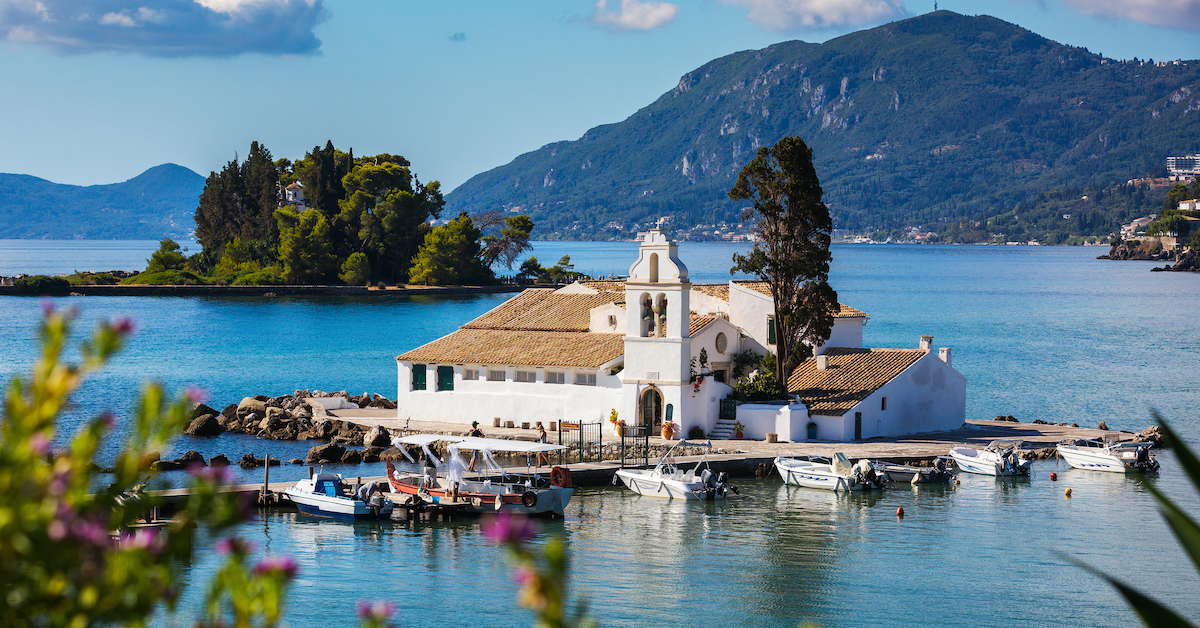 White-washed Vlacherna Monastery in the middle of a bay with mountains in the background