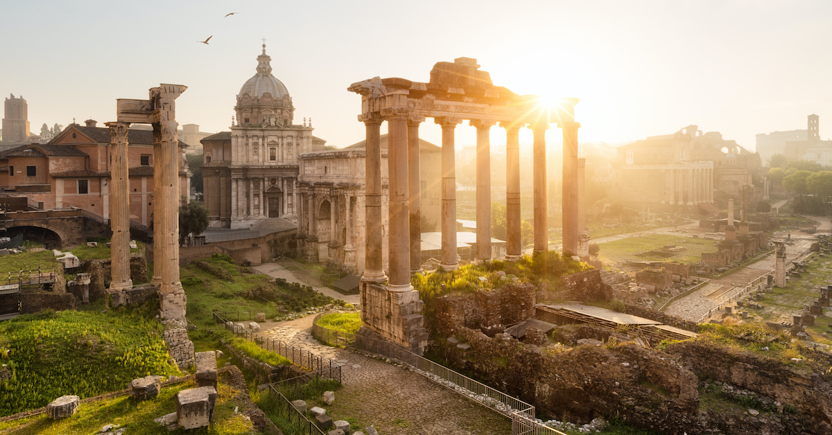 Sun shining over marble columns and a domed stone building in the Ancient Forum of Rome, one of the best family vacations with teens