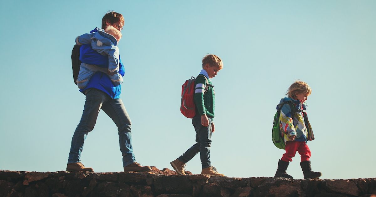 A man carrying a small child walking in line behind two other children wearing backpacks