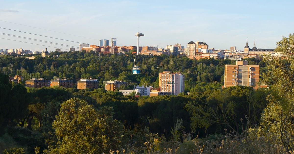 Cable car glides above the greenery of Casa de Campo with Madrid city buildings such as Plaza Mayor in the distance