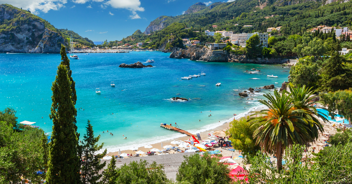 Greenery surrounding a bright blue bay with umbrella-speckled beaches around the coast in the Ionian islands, one of the less-trafficked Greece honeymoon destinations