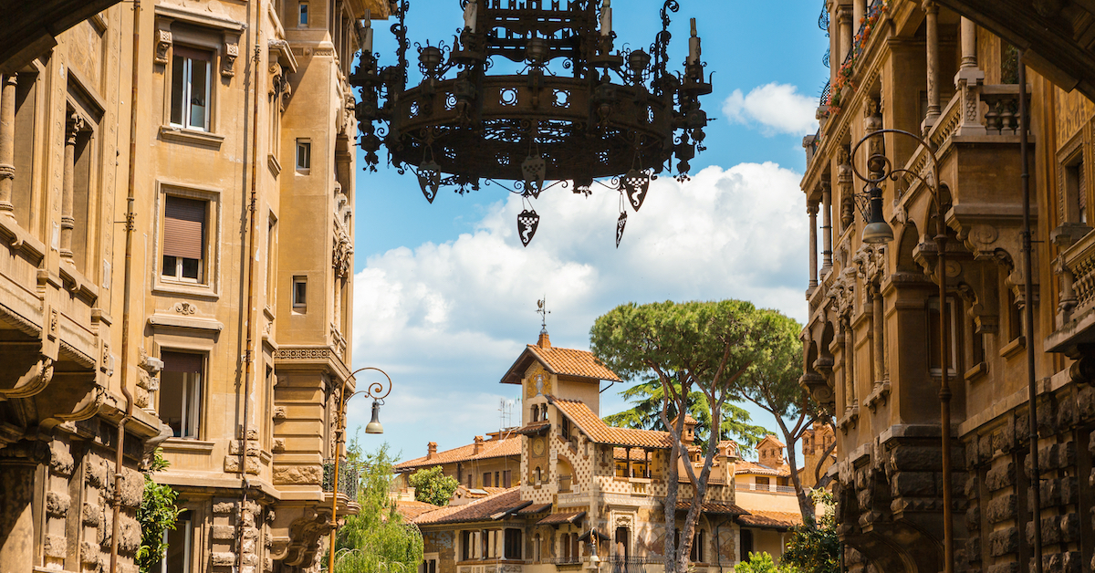 Metal chandelier hanging from an archway leading to the intricate stone buildings of Quartiere Coppede in Rome, Italy