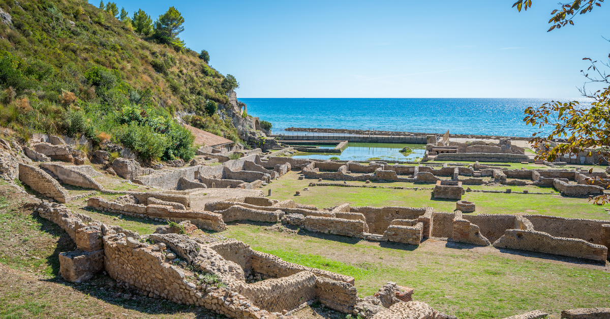 Short ruins scattered about grass with a cliffside on the left and ocean in the distance