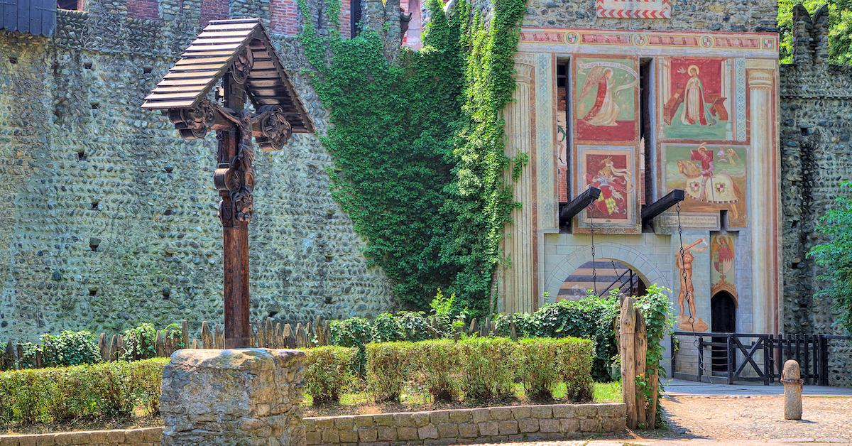 An old wooden crucifix with a medieval gate in a stone wall in the background