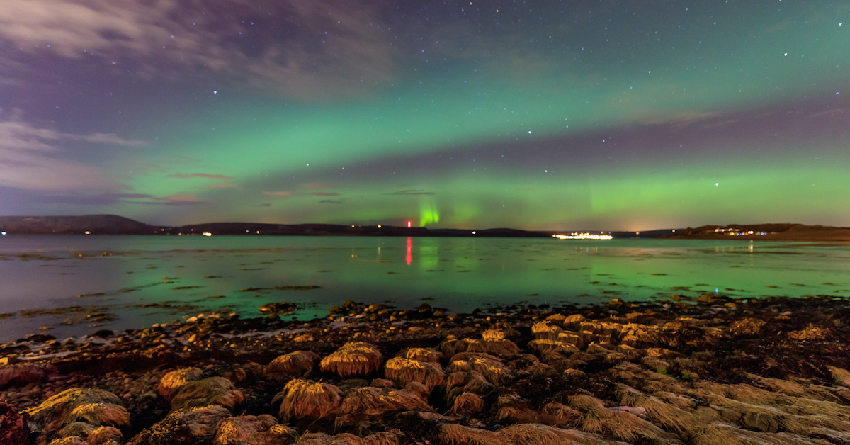 Aurora Borealis glowing over a lake with hills in the distance in the Scottish Highlands, a great place for stargazing in Europe
