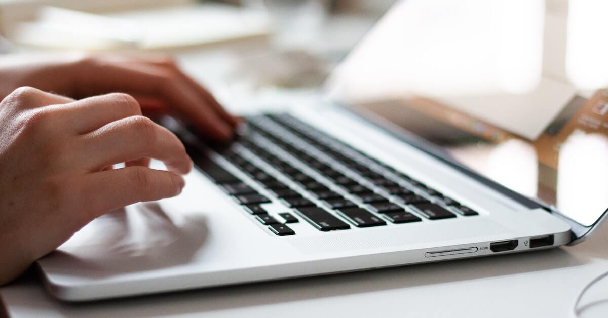 Close-up of hands typing on a laptop, as keeping on top of requirements is one of the most important post-pandemic travel tips