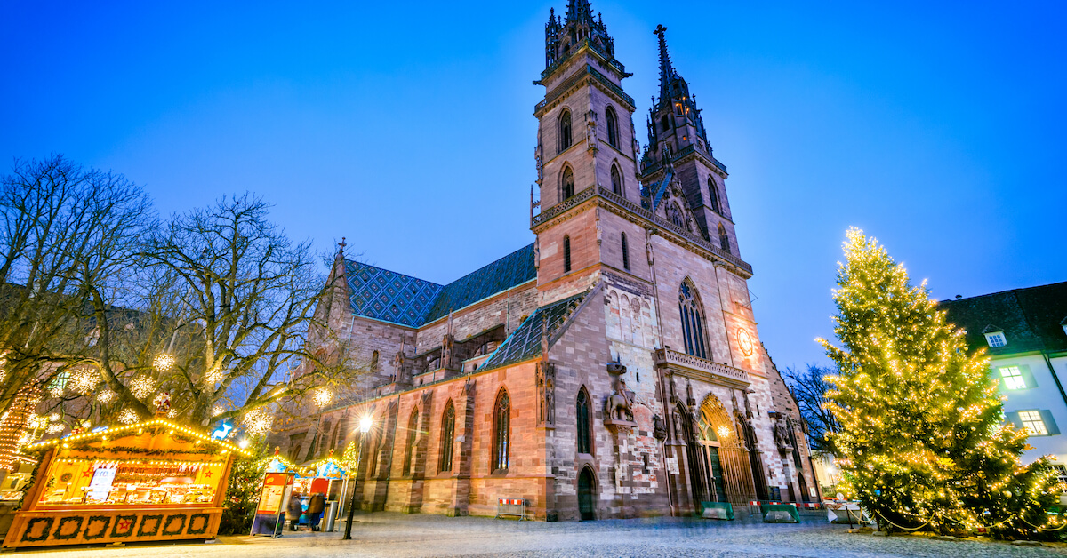 A stone cathedral with market stalls and a Christmas tree in front of it at night