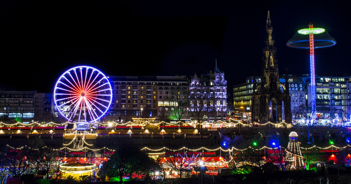 View across a river of a city skyline at night with a ferris wheel and holiday lights