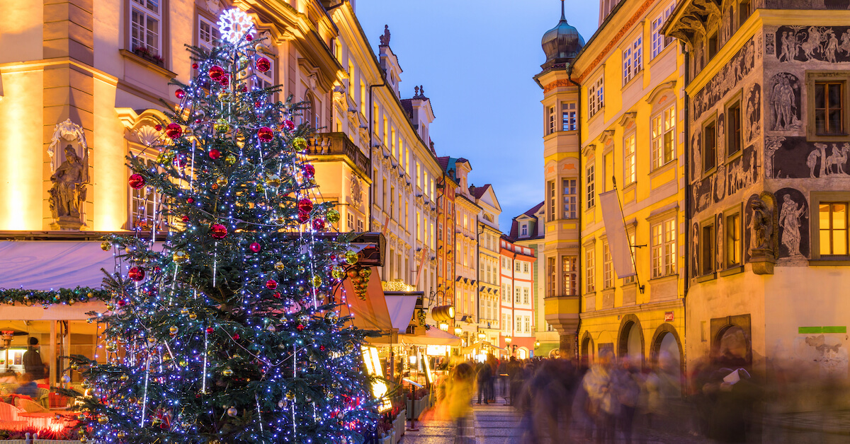 People walking on a city street lined with market stalls and a Christmas tree at night